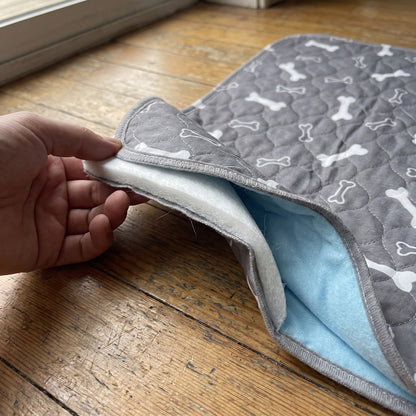Corner of the pad lifted to show the absorbent core and blue waterproof backing